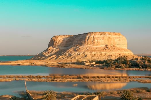 Eroded rock formation by a tranquil lake in a desert landscape, perfect for nature and travel photography.