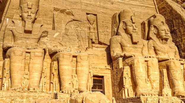 Sculptures of ancient Egyptian Pharaoh carved out of rock with decorative elements representing faces and clothes in sanctuary in Egypt