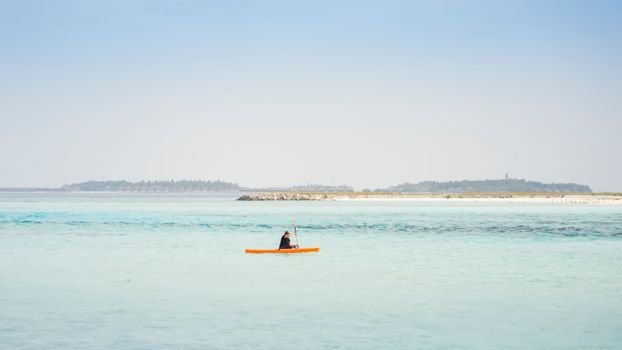 A person kayaking on the turquoise sea near Maafushi, Maldives with distant islands in view.
