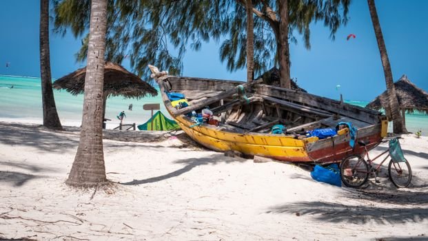 Tropical beach scene in Zanzibar featuring a colorful abandoned boat and bicycle under palm trees.