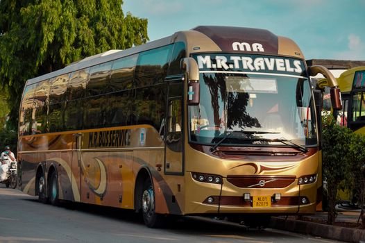 Golden luxury tour bus from M.R. Travels parked on street during the day with bright surroundings.