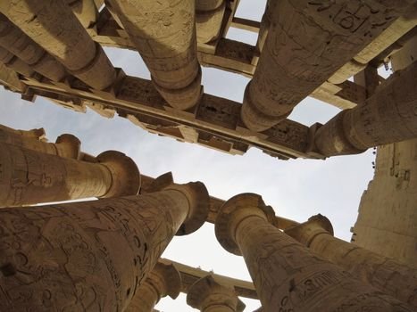 Upward view of ancient columns at Karnak Temple, showcasing intricate hieroglyphics.