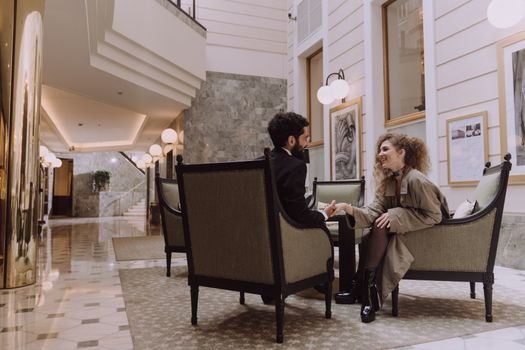 Couple sitting elegantly in a luxurious hotel lobby, exuding sophistication and style.