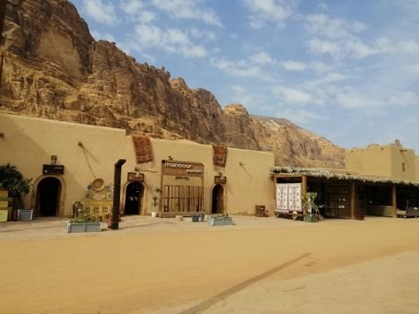 Adobe-style buildings set against dramatic rocky cliffs under a bright blue sky.