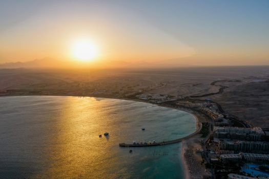 A breathtaking aerial sunset view over a calm coastal bay with distant desert backdrop.