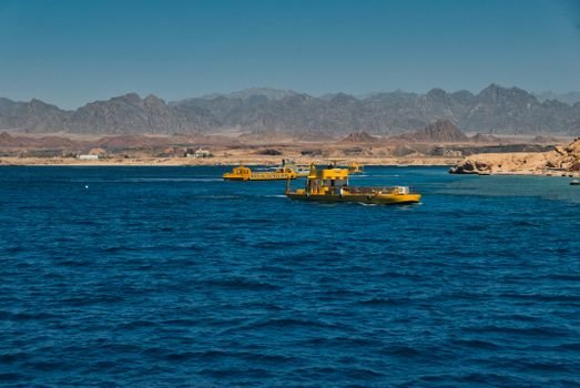 Yellow boats float on the vibrant blue waters of Ras Mohammed with scenic Egyptian mountains in the background.