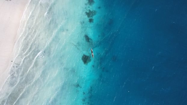 A drone captures a serene boat in the turquoise waters of Zanzibar, Tanzania from above.