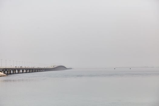 A scenic view of the King Fahd Causeway stretching over the calm sea on a foggy day in Bahrain.
