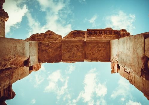 Low angle view of ancient Roman ruins against a blue sky with clouds.
