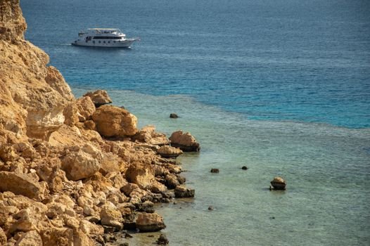 Eroded cliffs and a yacht on the clear blue sea create a serene coastal scene.