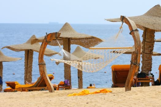 Tranquil beachside hammock under straw parasols with ocean view for perfect relaxation.