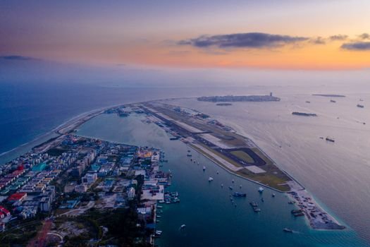 A stunning aerial view of a city with an airport runway by the ocean at twilight.