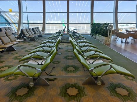 Modern airport seating area with green chairs and expansive windows offering a runway view.
