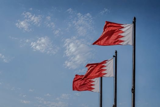 Three Bahraini flags fluttering against a clear blue sky in Manama, Bahrain.
