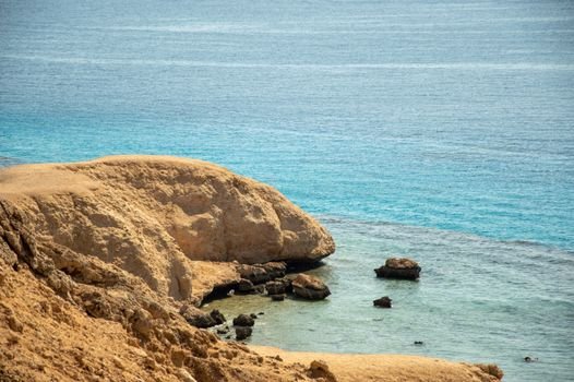 Peaceful coastal scene featuring sandstone cliffs and clear blue seawater under a summer sky.