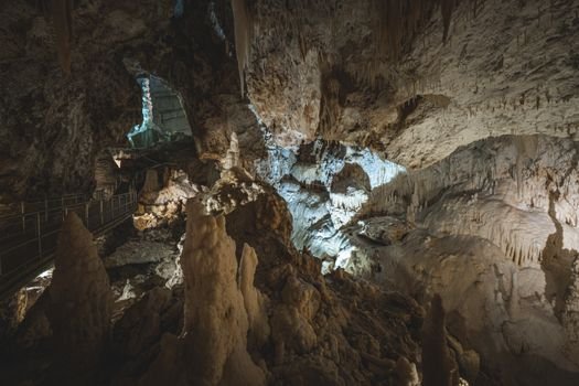 Explore the beauty of a large illuminated cave with stalactites and a rocky path, ideal for geology enthusiasts.