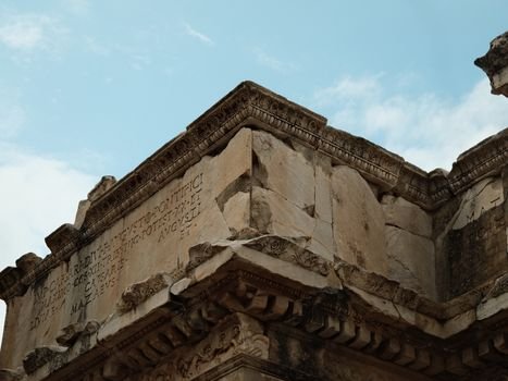 Detail of ancient Roman stone architecture featuring Latin inscriptions under a blue sky.