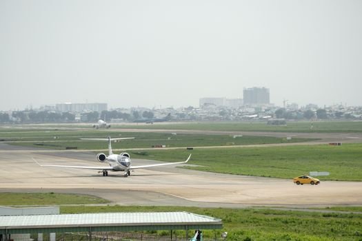 A private jet taxiing on the runway at an airport with a distant cityscape.