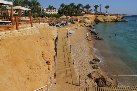 Sunny beach with wooden walkway and lounge chairs on a beautiful day.