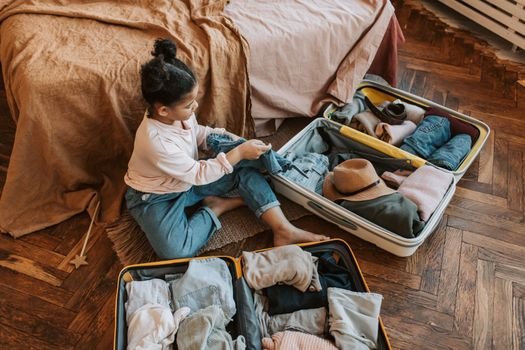 Young child sitting on bed packing a suitcase for an upcoming family vacation.