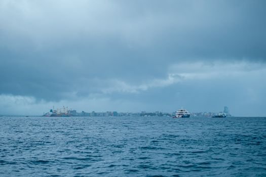 An expansive ocean with a cloudy sky, distant city skyline, and boats in view.