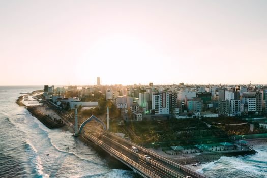 Modern Sinamale bridge with gates located near sea with waving sea and residential buildings in coastal town against cloudless sky
