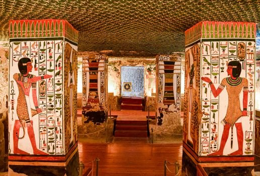 Interior of an ancient Egyptian tomb featuring vividly painted columns with hieroglyphics and murals.