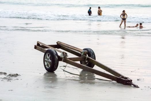 Rusty trailer on Langkawi beach with people enjoying the ocean in Malaysia.