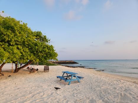 Serene beach view with turquoise waters and a picnic setup on Maafushi island, Maldives.