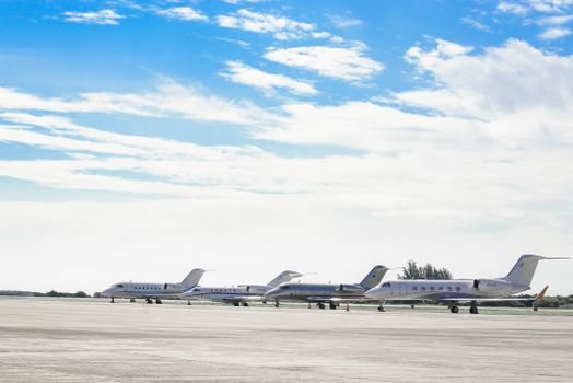 Row of private jets parked on a clear day at an open runway, showcasing aviation and luxury travel.