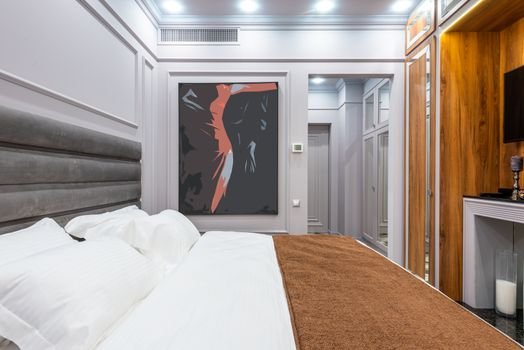 Contemporary hotel room interior with pillows and cover on bed against artwork on wall and light corridor