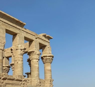 Stone columns of an ancient Egyptian temple under a clear blue sky in Aswan, Egypt.