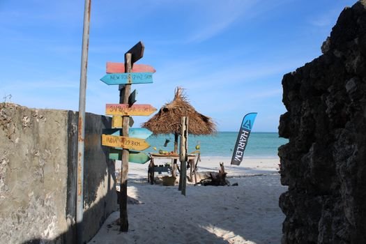 A vibrant signpost and straw hut on the sandy shores of Paje Beach, Tanzania.
