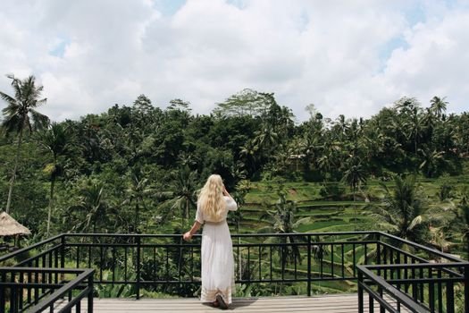 A woman with blonde hair overlooks a lush tropical forest from a balcony, capturing a serene and exotic travel moment.