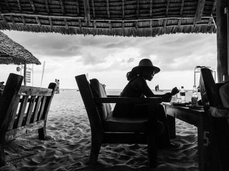 Black and white silhouette of a woman sitting in a beachside lounge at Kendwa, Tanzania.