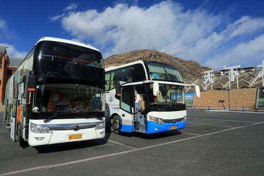 A pair of double-decker buses in a sunny mountain city setting under a clear blue sky.