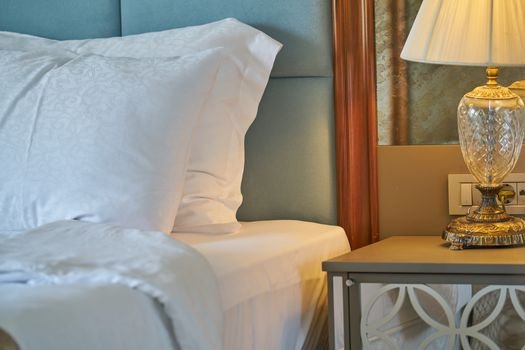 Elegant close-up of a comfortable bedroom setup with white linens and a decorative lamp.