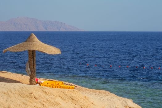 Serene beach with a straw parasol, sandy shore, and clear blue sea under a sunny sky.