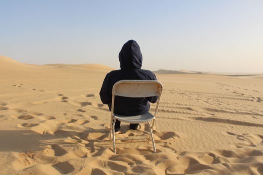 A lone person sits on a chair in the vast Siwa Oasis desert dunes, Egypt.