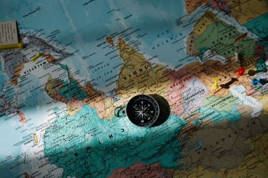 A compass placed on a detailed world map with colored push pins.