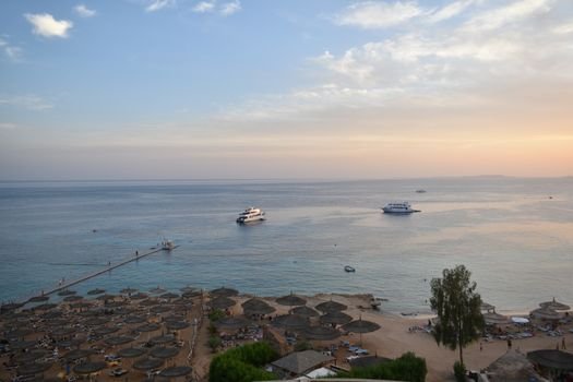 Stunning aerial view of Sharm El Sheikh's beach and sea during sunset with boats and parasols.