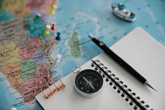 Flat lay of travel planning tools including a map, compass, notebook, and pen.