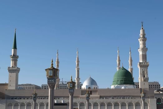 Iconic view of Al-Masjid an-Nabawi minarets against a clear blue sky in Medina, Saudi Arabia.