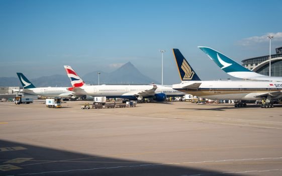 Multiple commercial airplanes parked at an airport terminal with a mountain view in the background.