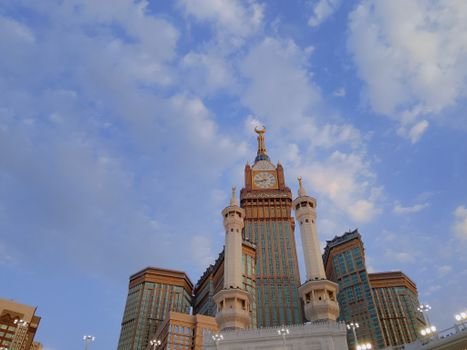 Majestic view of Abraj Al Bait Towers in Mecca with a clear blue sky and scattered clouds.