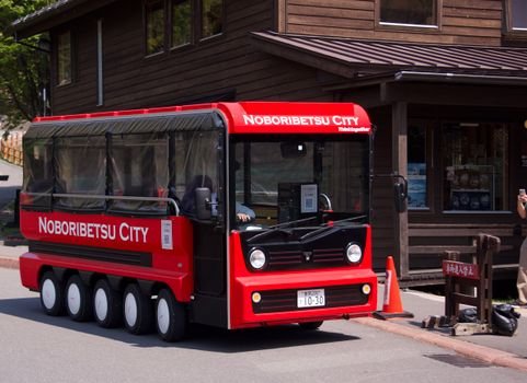Tourist bus in Noboribetsu City, Japan, parked in front of a wooden building on a sunny day.