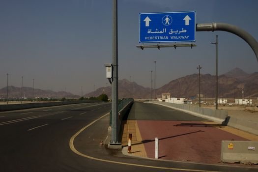 Road with pedestrian walkway sign, mountains in the background on a sunny day.