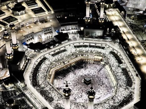 Stunning aerial photograph of the Grand Mosque in Mecca, illuminated at night, showcasing the Kaaba and worshippers.